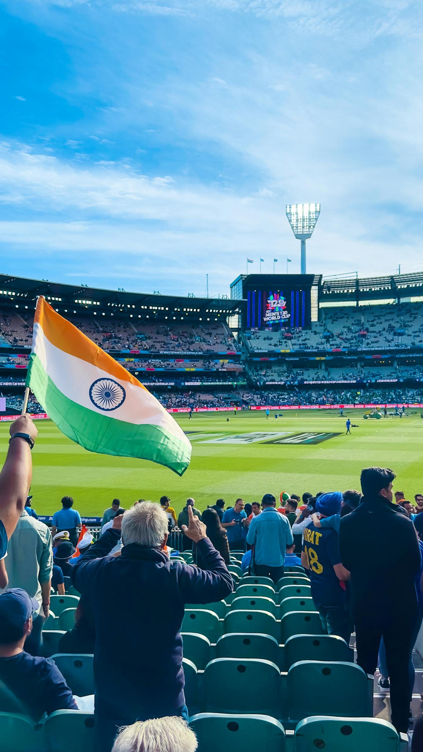 Excited fans waving the Indian flag at Melbourne Cricket Ground during a cricket match.